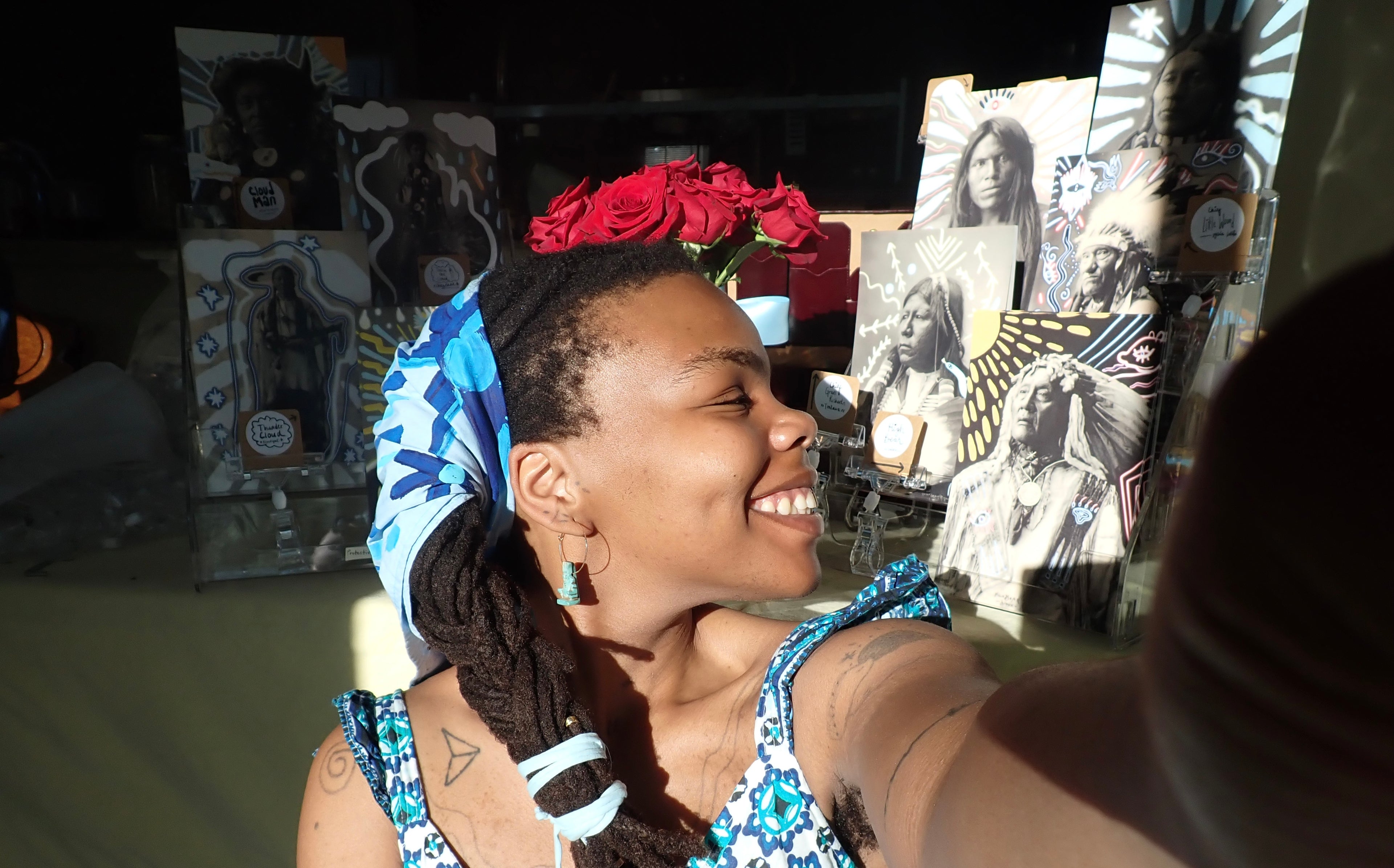 Woman with locs hair and evil eye bandana smiling in front of an altar with ancestor portraits.